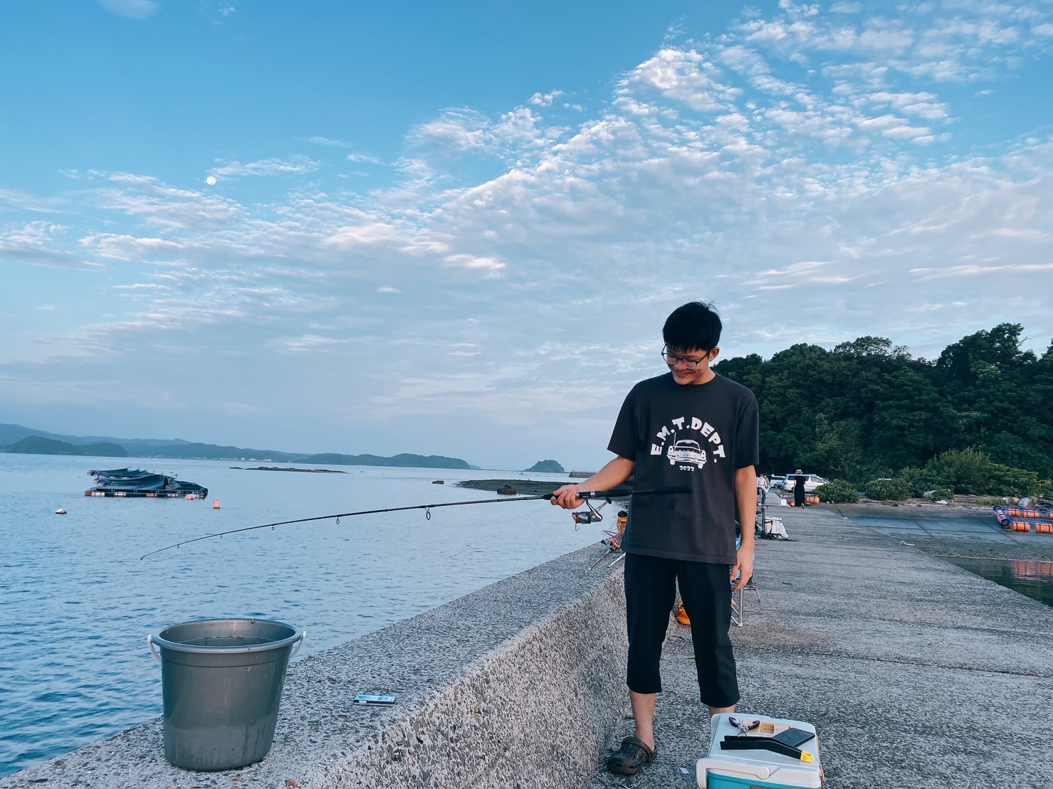 早朝の堤防で釣りをしています。青空が広がっています。